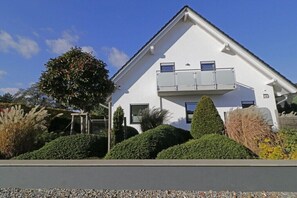 Ein modernes, zweistöckiges Gebäude mit Balkon, umgeben von gepflegten Hecken und einem Baum.