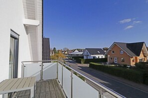 Eine Wohnstraße mit Häusern, einem Balkon mit Holzdeck und blauem Himmel.