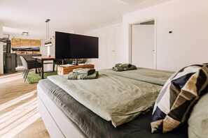 Ein modernes Zimmer mit Bett, Schreibtisch, Fernseher und Küchenzeile.