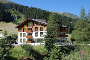 A multi-story building with a modern design, surrounded by lush greenery and mountains. - 3 in the Bohemia House (Gargellen)