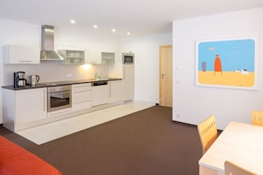 A modern kitchen with white cabinets, a built-in oven, and a microwave. There is a dining area with a table and chairs. - 3 in the Bohemia House (Gargellen)