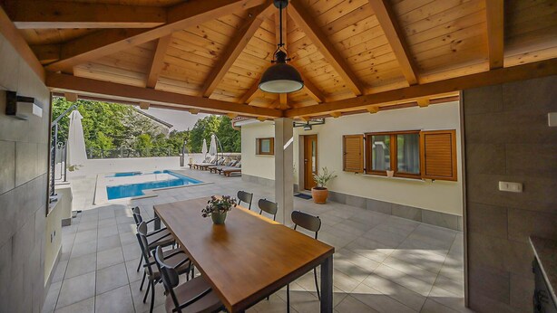 Eine überdachte Terrasse mit Pool, einem Esstisch und Stühlen sowie Blick ins Freie.