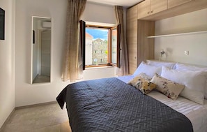 A bedroom with a bed, a window with curtains, a mirror, and a view of buildings outside. - Amazing home in Sapjane (Sapjane)