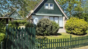 Ein grünes Haus mit einem dreieckigen Dach, einer Veranda und einem weißen Zaun.