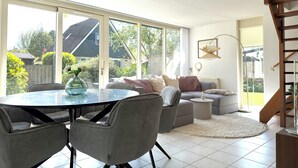 Ein geräumiges Zimmer mit großen Fenstern, einer Essecke, einer Couch und einer Treppe.