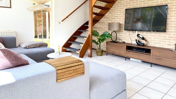 Ein modernes Wohnzimmer mit einem grauen Sofa, einer Holztreppe, einem Fernseher und einer Ziegelwand.