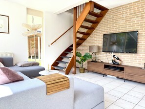 Un salon moderne avec un canapé gris, un escalier en bois, un téléviseur et un mur en briques.