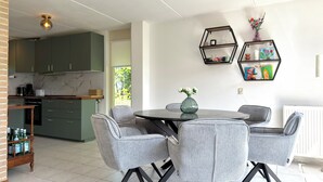 Eine moderne Küche mit grünen Schränken, ein Essbereich mit grauen Stühlen und sechseckigen Regalen an der Wand.