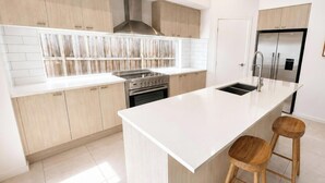 A modern kitchen with light wood cabinets, a stainless steel range hood, a double sink, and a built-in oven. - Wagtail Whispers - Spacious Coastal Escape (Catherine Hill Bay)