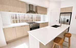 Eine moderne Küche mit hellen Holzschränken, einer Edelstahl-Dunstabzugshaube, einer Spüle mit zwei Becken und einem Einbauofen.