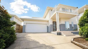 A two-story house with a front garage, a balcony, and a well-maintained lawn. - Wagtail Whispers - Spacious Coastal Escape (Catherine Hill Bay)