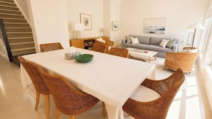 A dining area with a table and chairs, a sofa, a lamp, and a staircase. - Wagtail Whispers - Spacious Coastal Escape (Catherine Hill Bay)