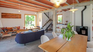 A spacious living area with a wooden dining table, a sofa, and a staircase leading to another level. - Bastide Néo Provencale (Grignan)