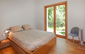 A bedroom with a bed, a chair, a bedside table, and a window with a view of greenery. - Bastide Néo Provencale (Grignan)