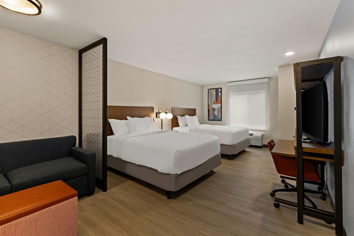 A hotel room with two beds, a sofa, a desk, and a TV.