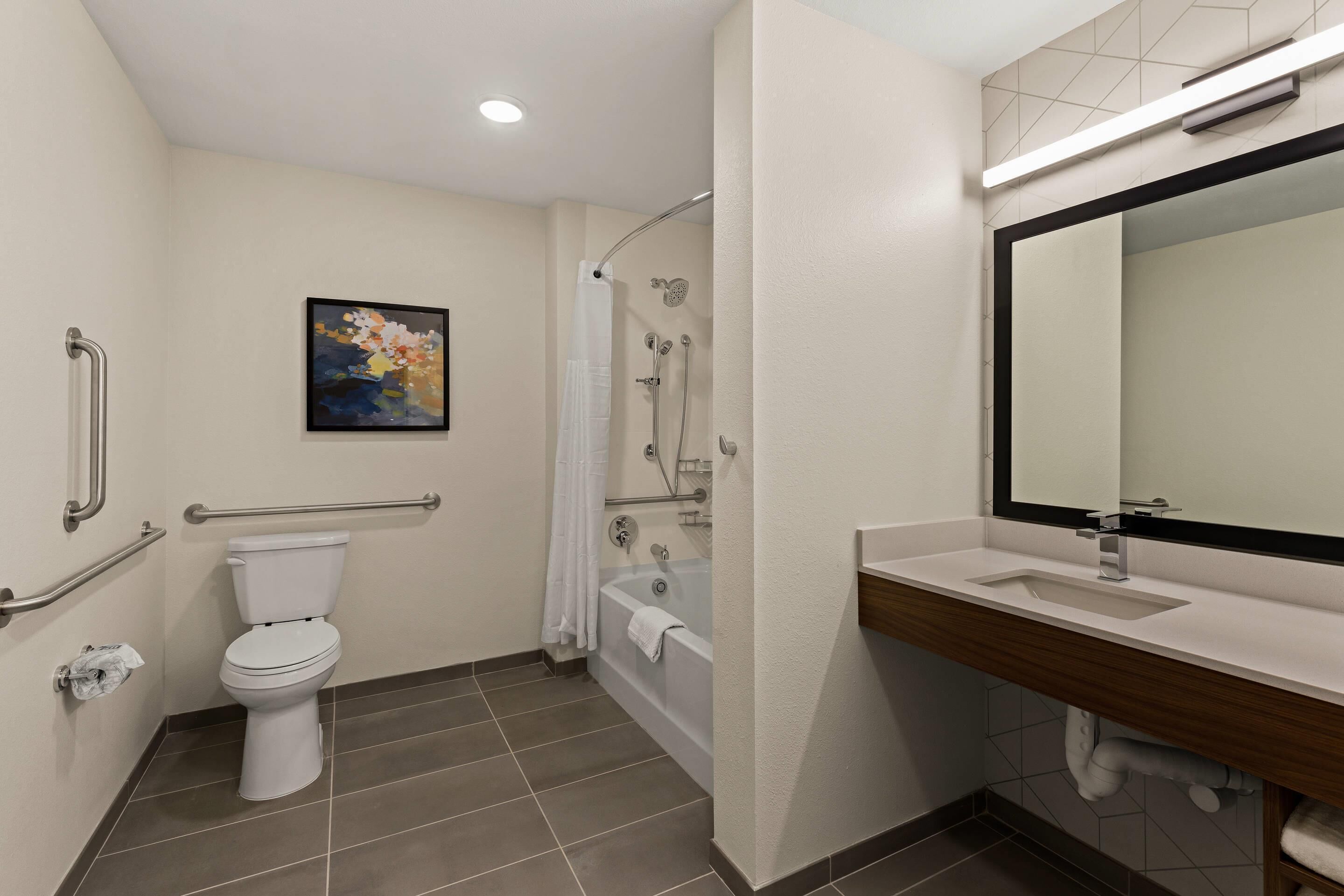 Ein Badezimmer mit Toilette, Badewanne und Waschbecken, ausgestattet mit Haltegriffen und einer Dusche.