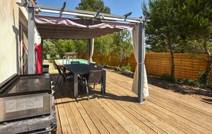 An outdoor patio with a grill, a table, and chairs, surrounded by a wooden deck and a pool. - Gorgeous home in Mérindol (Mérindol)