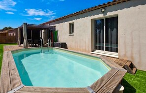 A rectangular swimming pool with a wooden deck, a covered patio area, and a sliding glass door. - Gorgeous home in Mérindol (Mérindol)