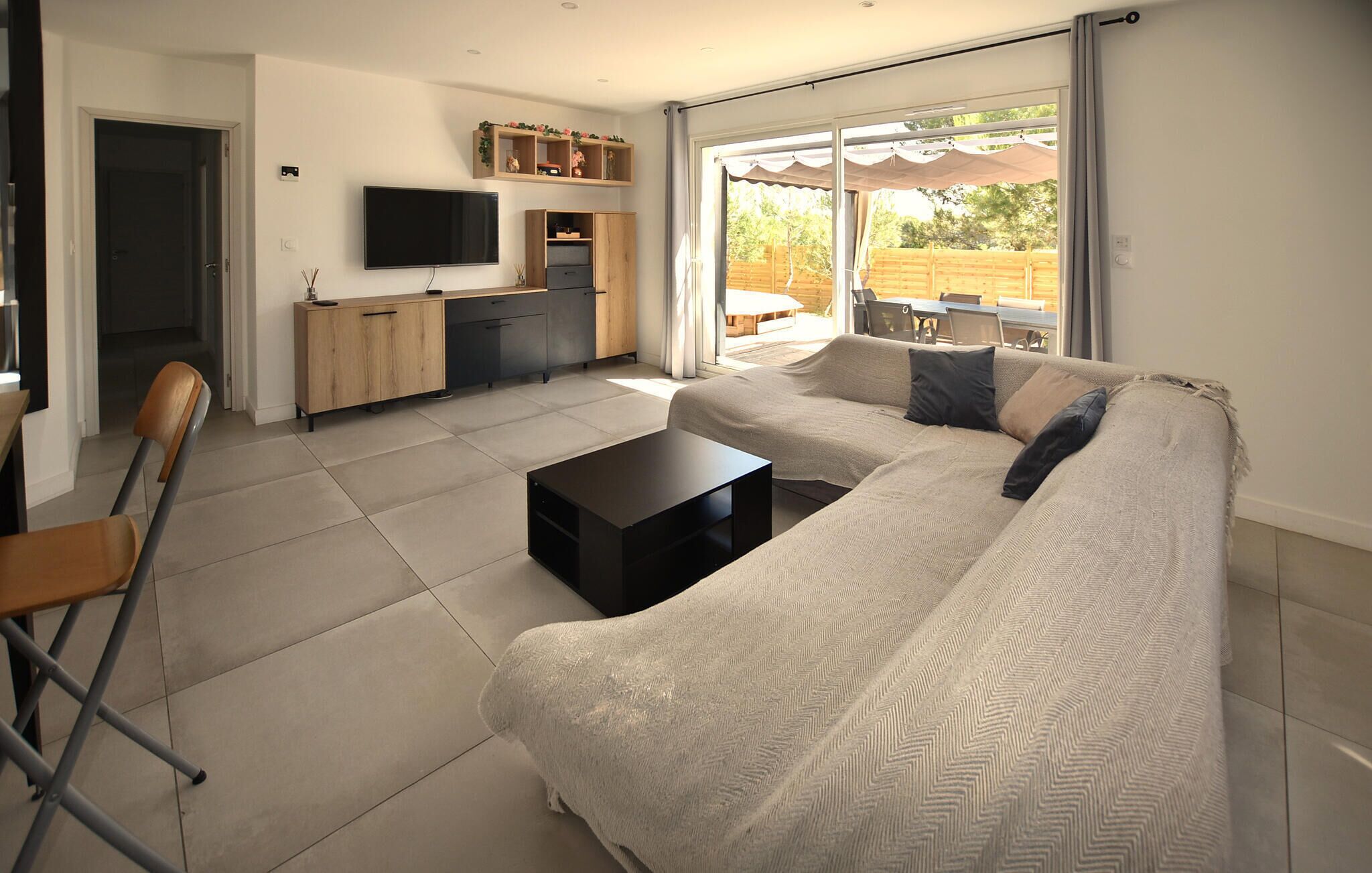 Una sala de estar moderna con un sofá, una mesa de centro y un televisor. Hay una puerta corredera de vidrio que da a un espacio al aire libre.