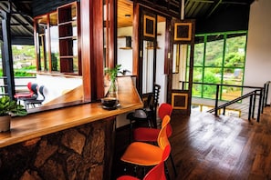 A bar area with a stone counter, red chairs, and a view of greenery through large windows.