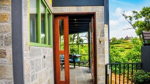 Un edificio in pietra con una porta di legno, un balcone con una sedia e vista su un paesaggio verde.