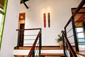 Un escalier avec des marches en bois et des rampes en métal, menant à une pièce dont un mur est blanc et où se trouve une plante.