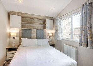 Ein Hotelzimmer mit Bett, Nachttischen, einem Fenster mit Vorhängen und einer Heizung.