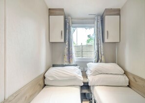 Ein schmales Zimmer mit zwei Betten, einem Fenster mit Vorhängen und einer Holzbalkendecke.