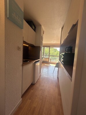 Eine schmale Küche mit Holzboden, weißen Schränken, einem eingebauten Ofen und einer Kaffeemaschine auf der Arbeitsplatte.
