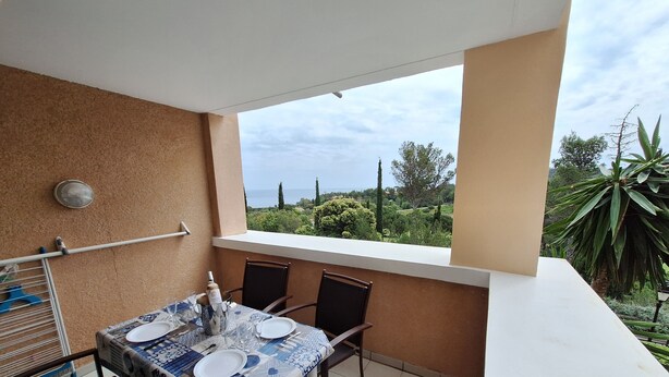 Un balcon avec une table dressée pour deux personnes, un étendoir et une vue sur la mer et la verdure.