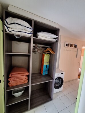 Un cuarto de lavandería con una lavadora, un estante con toallas dobladas y una bolsa colgada en un perchero.