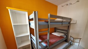Un lit superposé avec une étagère, une petite table et un luminaire fixé au mur, dans une pièce aux murs orange.