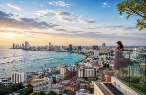 A cityscape with a high-rise building overlooking a coastal area with boats. - 1 BR Sea View Condo Near Walking Street (ตำบล หนองปรือ)