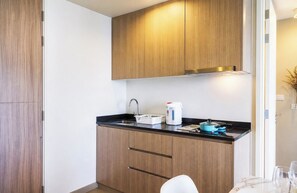 Een compacte keuken met houten kastjes, een zwart aanrecht en een kleine eethoek met een witte stoel.