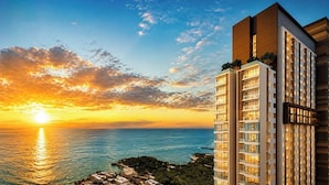 A high-rise building with multiple balconies, a sunset view, and a body of water in the background. - 1 BR Sea View Condo Near Walking Street (ตำบล หนองปรือ)
