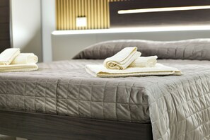 A neatly made bed with a quilted grey duvet, pillows, and folded towels. - BorgoNaro, an authentic oasis of peace located in the charming village of Dattilo. (Dattilo)