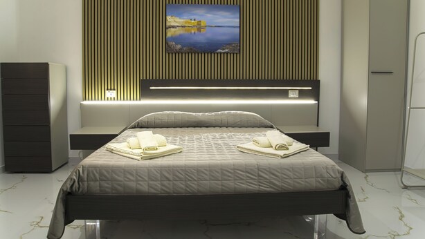 Een moderne slaapkamer met een bed, nachtkastjes, een tv aan de muur en een groot raam.