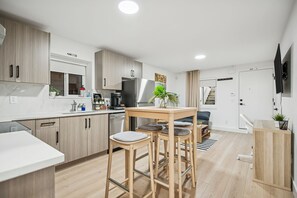 Eine moderne Küche mit Holzschränken, einem Essbereich mit Hockern, einem eingebauten Backofen und einem an der Wand befestigten Fernseher.