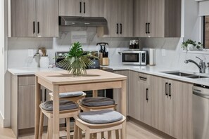 Eine moderne Küche mit Holzausstattung, einem Esstisch mit gepolsterten Hocker, einer Mikrowelle und einem Spülbecken.
