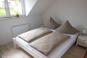 Ein Schlafzimmer mit einem Bett, Kissen, einem Nachttisch, einer Lampe, einem Fenster mit Ausblick und einer Heizung.