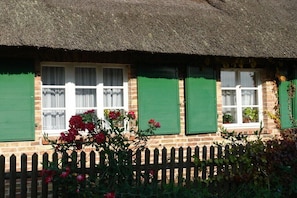 Ein traditionelles Backsteinhaus mit einem Reetdach und grünen Fensterläden.