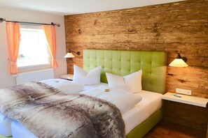 Ein Schlafzimmer mit einem grünen, gepolsterten Kopfteil, weißer Bettwäsche, einem Fellüberwurf und holzverkleideten Wänden.