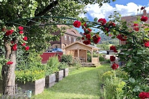 Ein Garten mit einer Holz-Pergola, einem roten Gebäude und einem klaren Himmel.