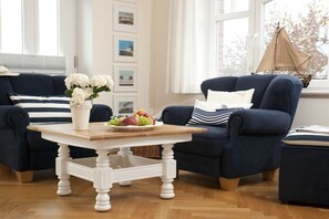 Ein Wohnzimmer mit zwei dunkelblauen Sofas, einem weißen Couchtisch und einer Wand mit gerahmten Bildern.