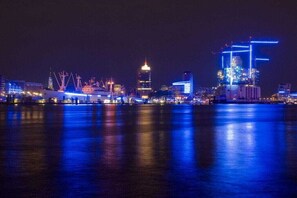 Ein beleuchtetes Stadtbild bei Nacht mit Gebäuden und einem sich spiegelnden Gewässer.