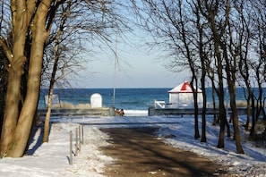 A snow-covered pathway leading to a coastal area with a lighthouse and a bench. - 22, Residenz Seestern (Kühlungsborn-West)