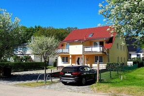 Ein zweistöckiges Haus mit rotem Dach, einem Balkon und einem parkenden Auto.