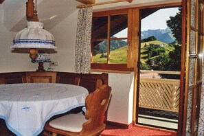 Ein Zimmer mit Esstisch, Stuhl, Lampe, Fenster mit Blick auf eine Berglandschaft und einem Balkon mit Holzgeländer.
