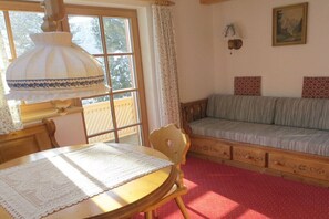 Ein Zimmer mit Holztisch, einer Couch, einem Fenster mit Vorhängen und einer Wandlampe.