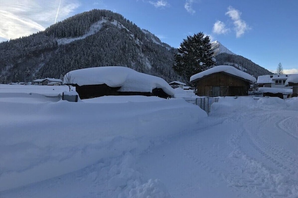 A snow-covered village with wooden buildings, a mountain in the background, and a clear sky.